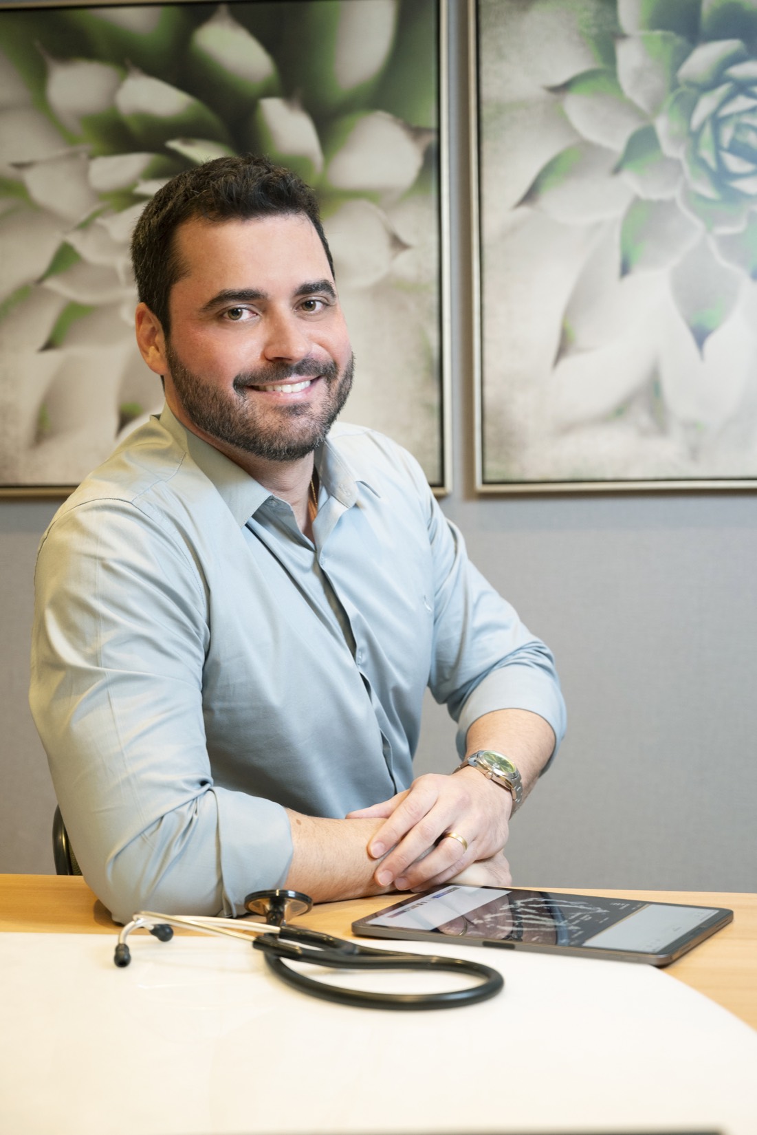 Dr. Marcio Machado, médico, sorrindo em seu consultório em Cachoeiro de Itapemirim/ES